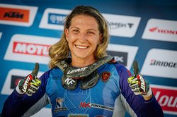 Das Bild zeigt eine Motocrossfahrerin vor der Siegerehrung. Sie hebt beide Daumen hoch.